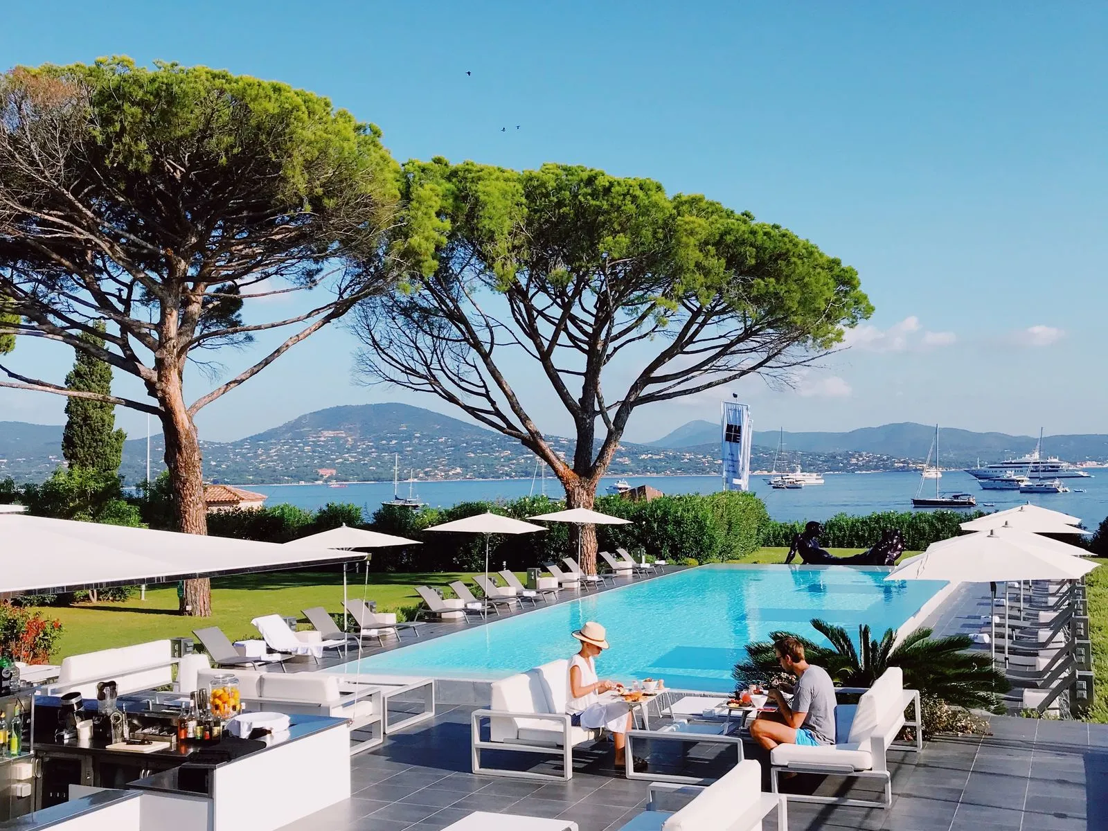Resort pool framed by umbrella pines above a Mediterranean bay