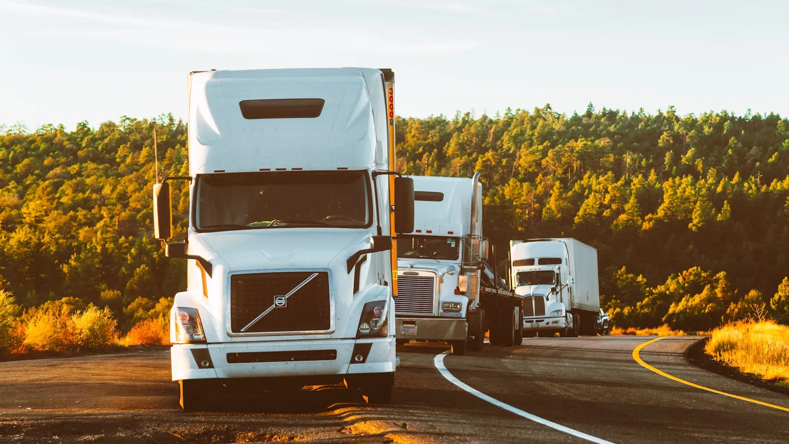 Convoy of semi-trucks traveling along a scenic highway